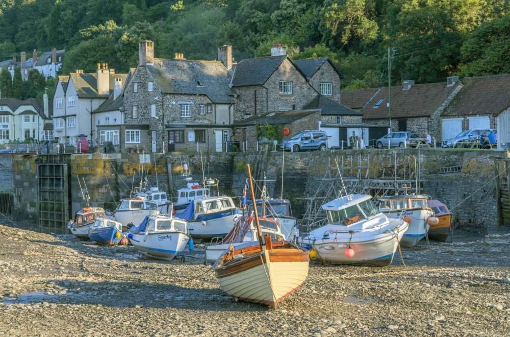 Porlock Weir, UK - July 24, 2012: Boats moored in the harbour of the fishing port of Porlock Weir on the North Somerset coast. It is low tide and the boats are beached on the shingle. There is the village the other side of the harbour with tourists and residents and it is a warm sunny evening in summer.